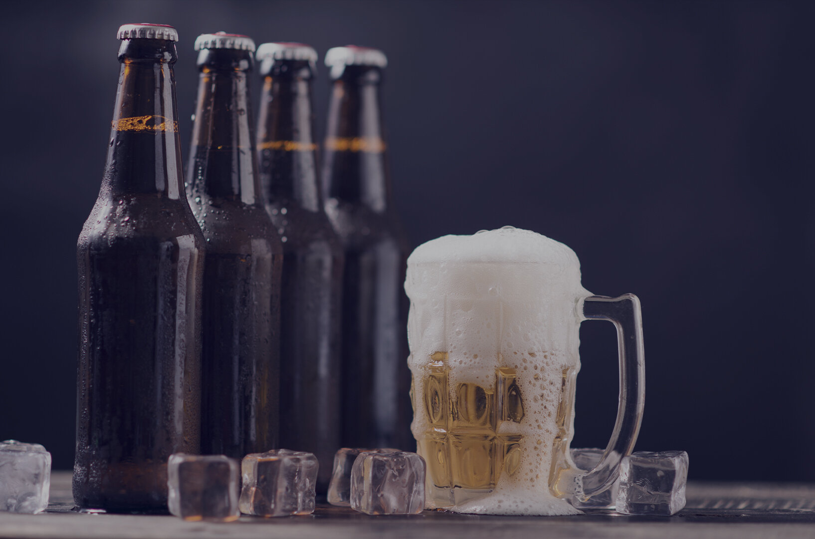 beer in glass pouring foam next to ice cubes and bottles